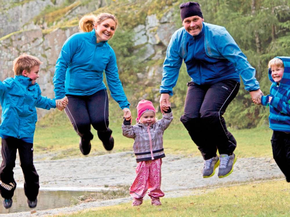 Barn og voksne leker og hopper sammen utendørs i en park eller skogsområde.