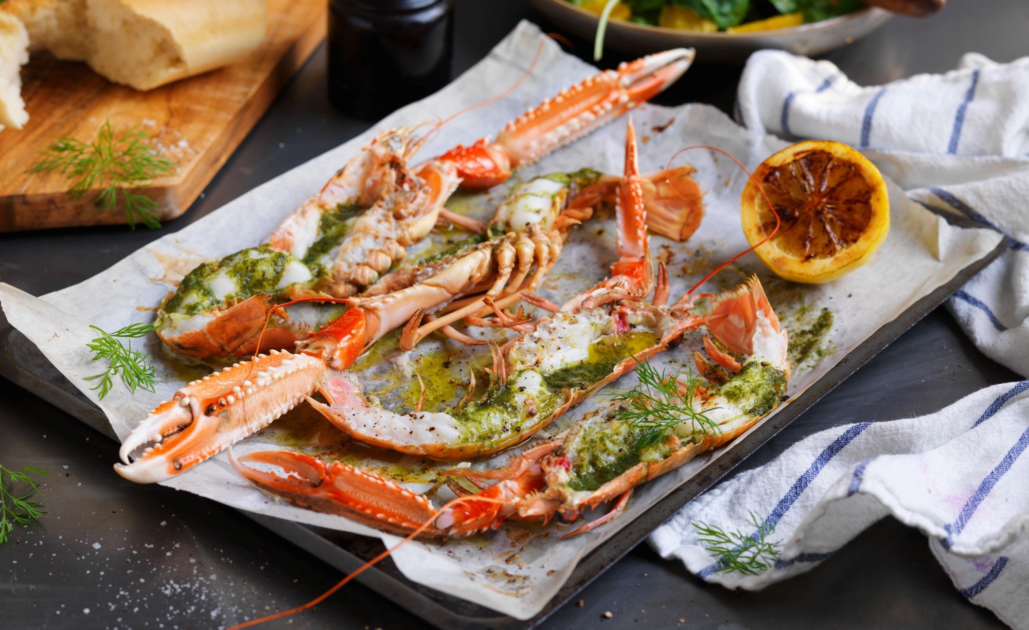 Gratinerte sjøkreps med ramsløksmør servert på et fat med sitronbåt og urter, klar til å nytes.