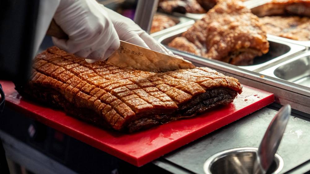 En person skjærer i en stor, grillet ribbe på et kjøkkenbord med kjøttfat i bakgrunnen.