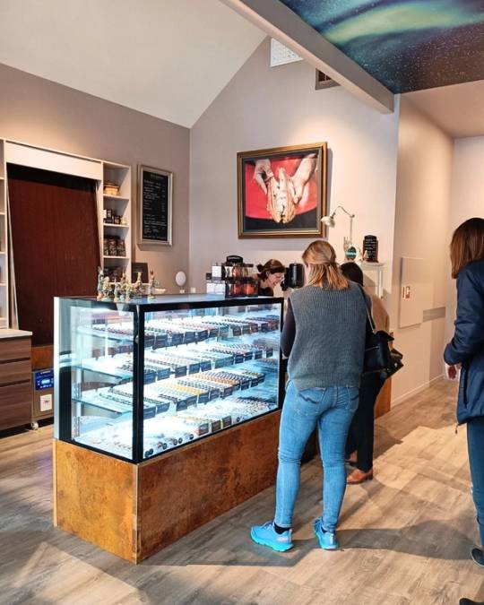 Kunder står foran en iskremdisk i en butikk, med et kunstverk av en hånd med blomster på veggen bak.