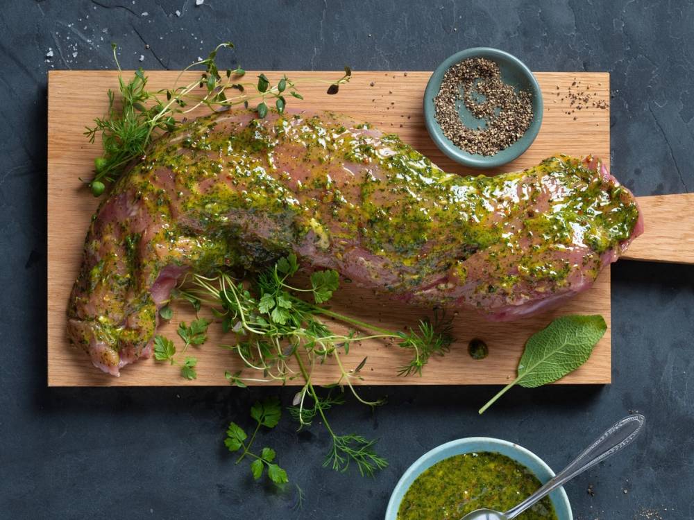 Svinefilet med urter og krydder på et skjærebrett med en liten skål med saus ved siden av.