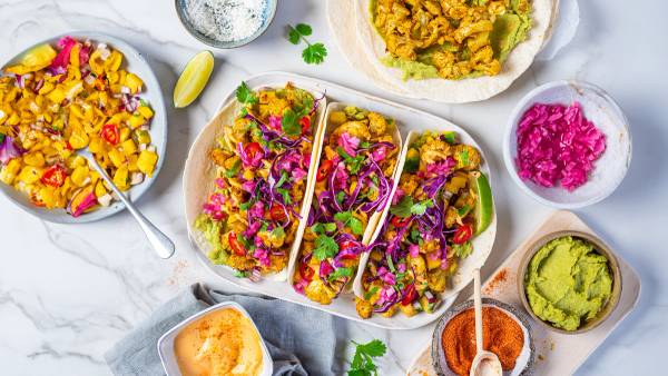 Blomkål taco med fargerike grønnsaker og krydder, servert på en hvit tallerken med tilbehør rundt.