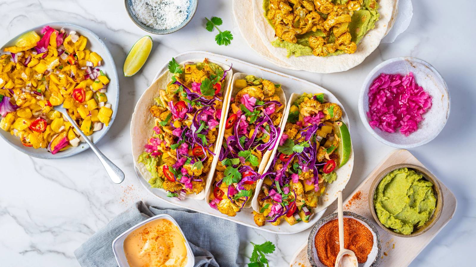 Blomkål taco med fargerike grønnsaker og krydder, servert på en hvit tallerken med tilbehør rundt.