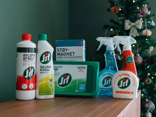 Ulike rengjøringsprodukter og en sprayflaske står på et bord foran en julegran med pynt.