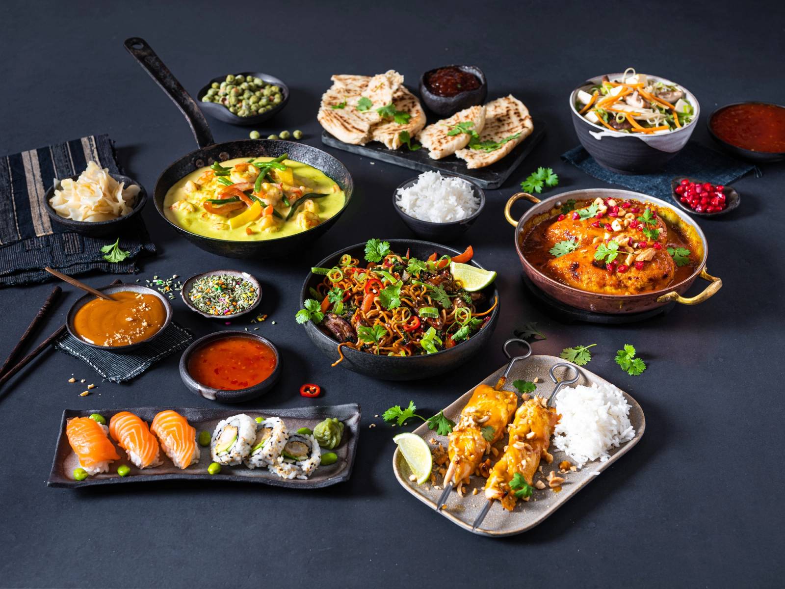 Et utvalg av asiatisk mat, inkludert sushi, suppe, risretter og småretter, på et svart bord.