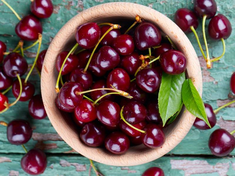 Moreller i en treskål med noen grønne blader på en treflate