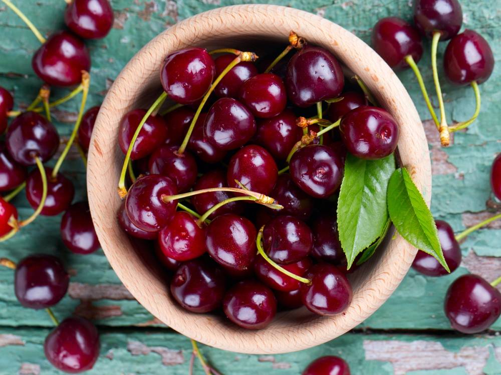 Moreller i en treskål med noen grønne blader på en treflate