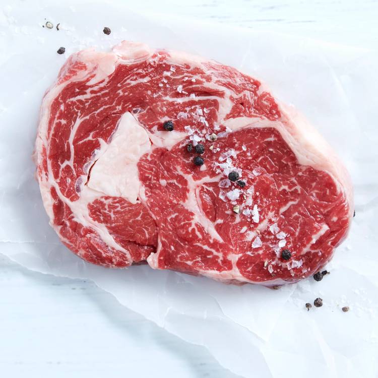 En rå entrecôte med marbling og noen svarte pepperkorn på, liggende på hvitt papir.
