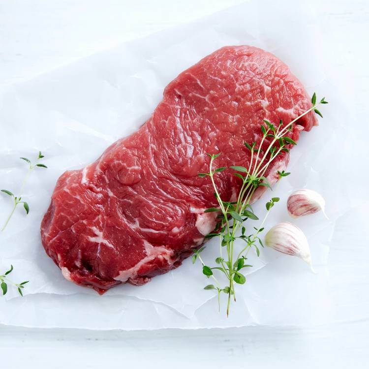 En rå ytrefilet av storfe med hvitløk og frisk timian på et hvitt papirark.