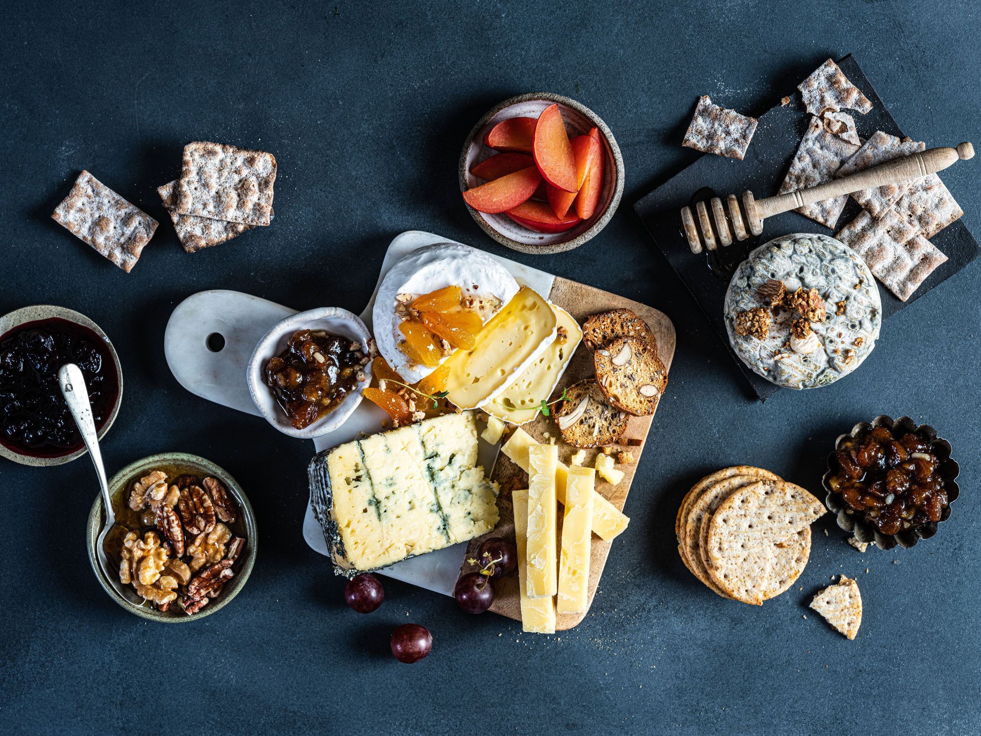 Et ostefat med ulike typer ost, kjeks, honning, nøtter og tørket frukt på en mørk bakgrunn.