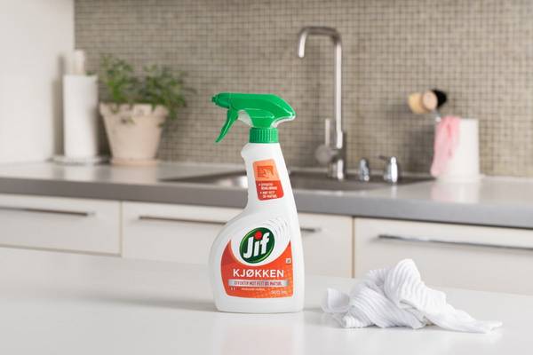 En sprayflaske med Jif kjøkkenspray står på kjøkkenbenken foran en vask og kjøkkenutstyr.