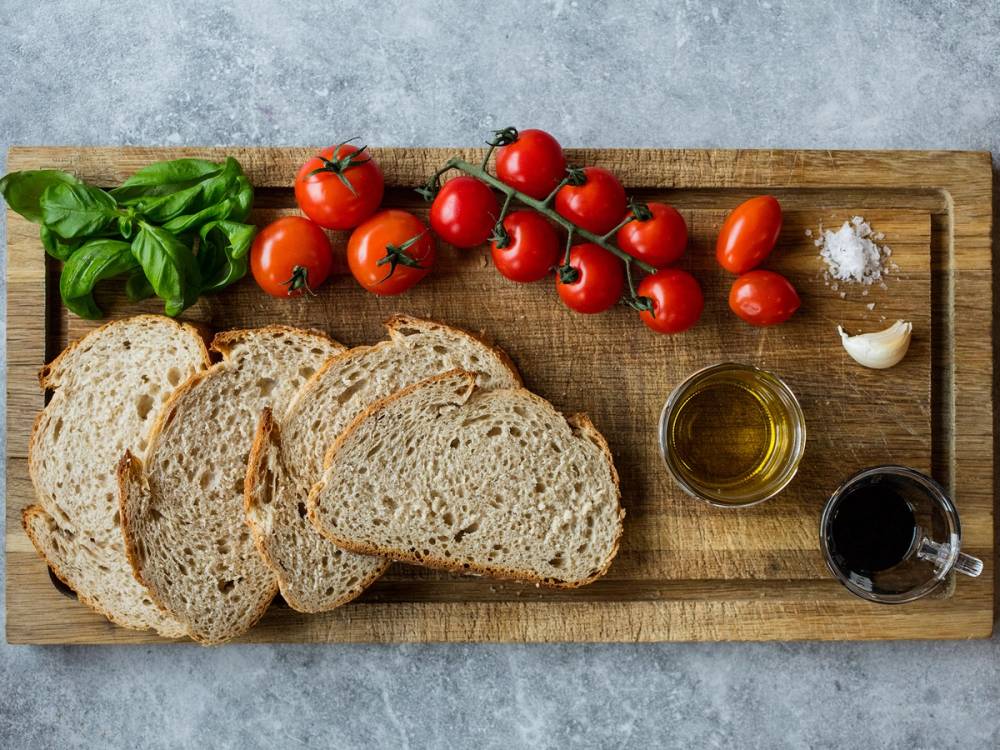 Skarpe tomater, fersk basilikum, og tre skiver brød med olivenolje og balsamico på et trebrett.