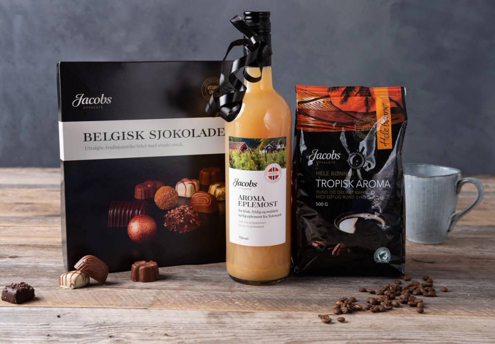 Ulike Jacobs-produkter, inkludert belgisk sjokolade, juice og kaffe, på et bord med en kopp i bakgrunnen.