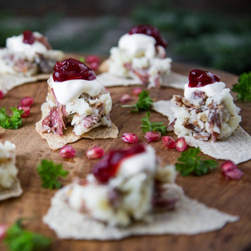 Pinnekjøtt og brandade servert som små porsjoner på et fat med pynt av granateplefrø og urter