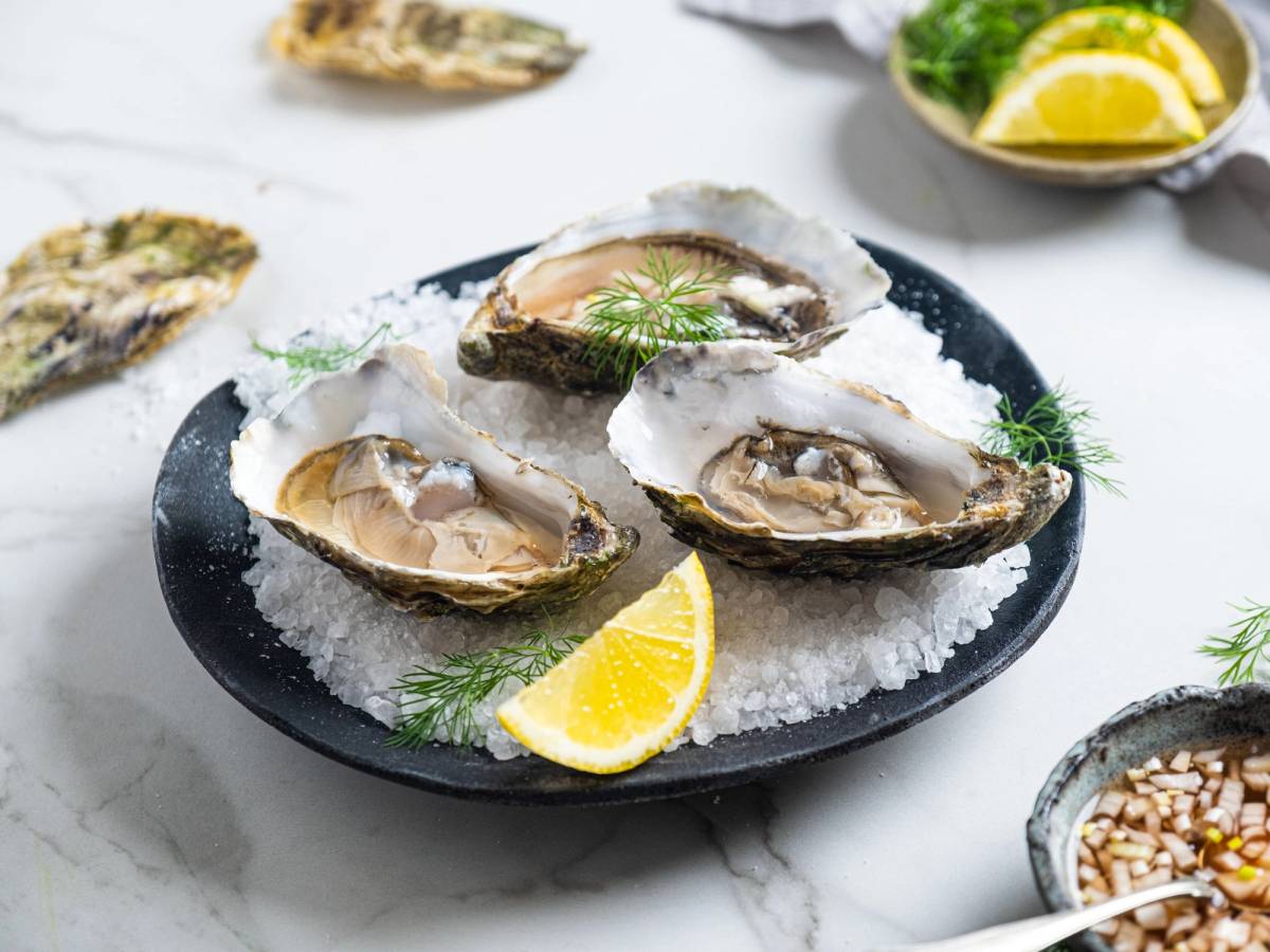 Østers på en svart tallerken med sitronbåter og dill, omgitt av andre sjømatretter og tilbehør.
