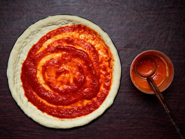 En pizzabunn med tomatsaus fordelt på toppen, klar for å bli bakt.