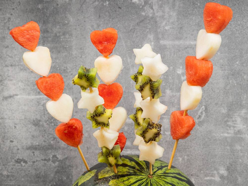 Fruktspyd med jordbær, kiwi og marshmallows på en grå bakgrunn, sannsynligvis til en babyshower.