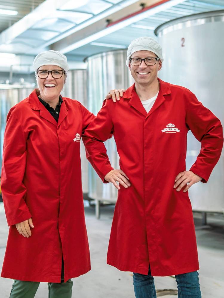 To personer i røde arbeidsfrakker står sammen i en industriell setting, med en person som har armen rundt den andre.