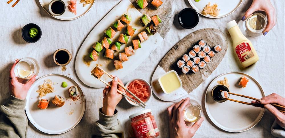 Sushibiter på tallerkener med soyasaus og spisepinner, sett på et bord med ulike småretter og drikke.