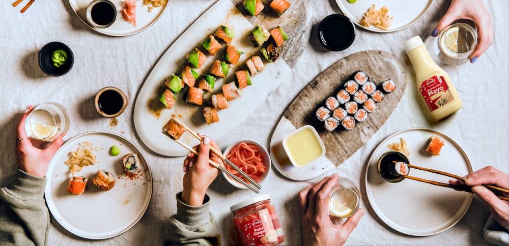 Sushibiter på tallerkener med soyasaus og spisepinner, sett på et bord med ulike småretter og drikke.