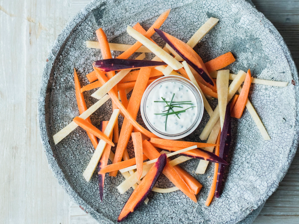 Oppkuttede gulrot- og kalrotstaver med urtedip i midten på en steinplate