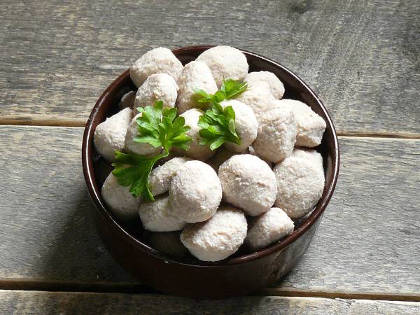 Små hvite kaker eller konfekt i en skål med noen grønne blader på toppen, plassert på en treflate.