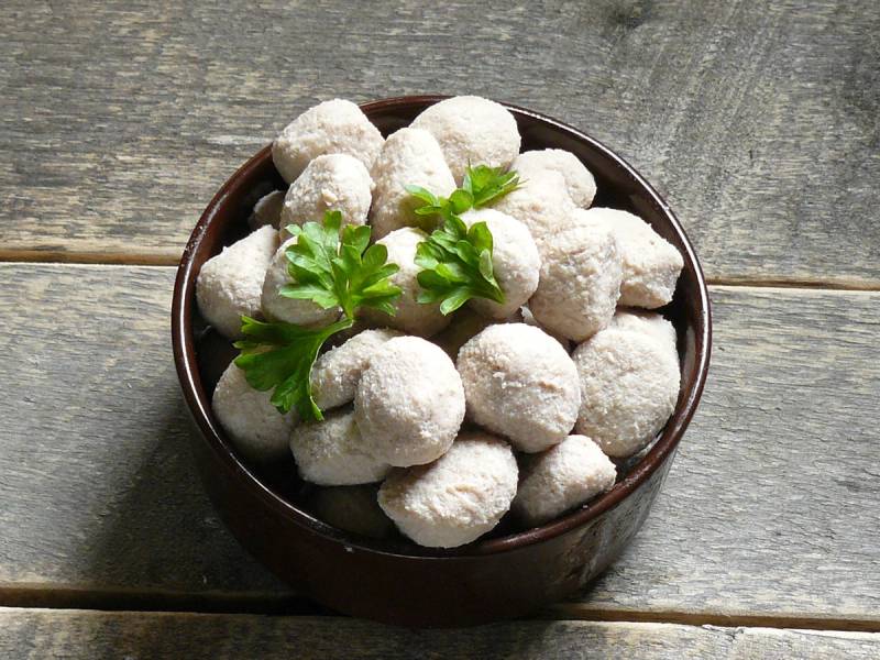 Små hvite kaker eller konfekt i en skål med noen grønne blader på toppen, plassert på en treflate.