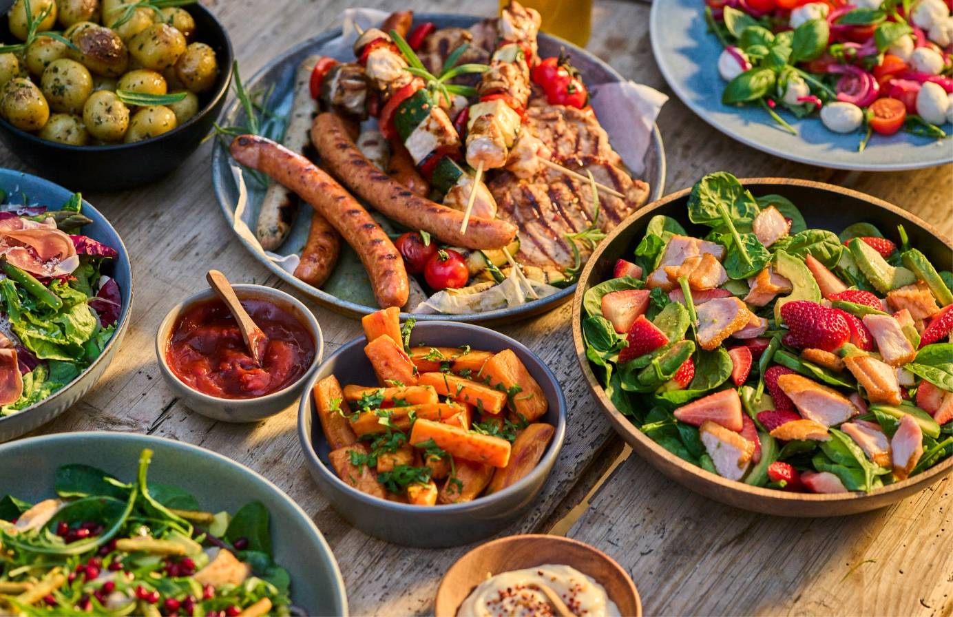 Et utvalg av ulike salater og småretter på tallerkener og i boller, inkludert grønnsaker, frukt og dipper.