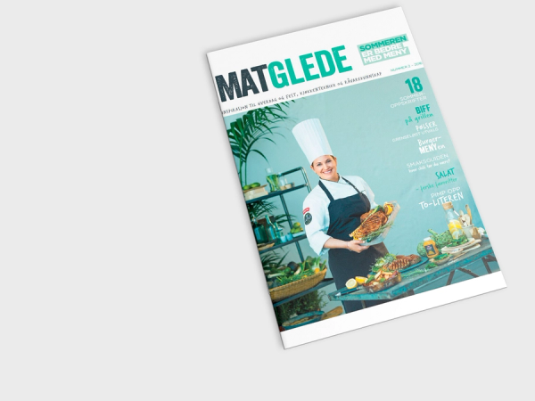 En kokk i hvit kokkehatt og forkle som lager mat på kjøkkenet med grønnsaker og kjøtt på benk foran seg.