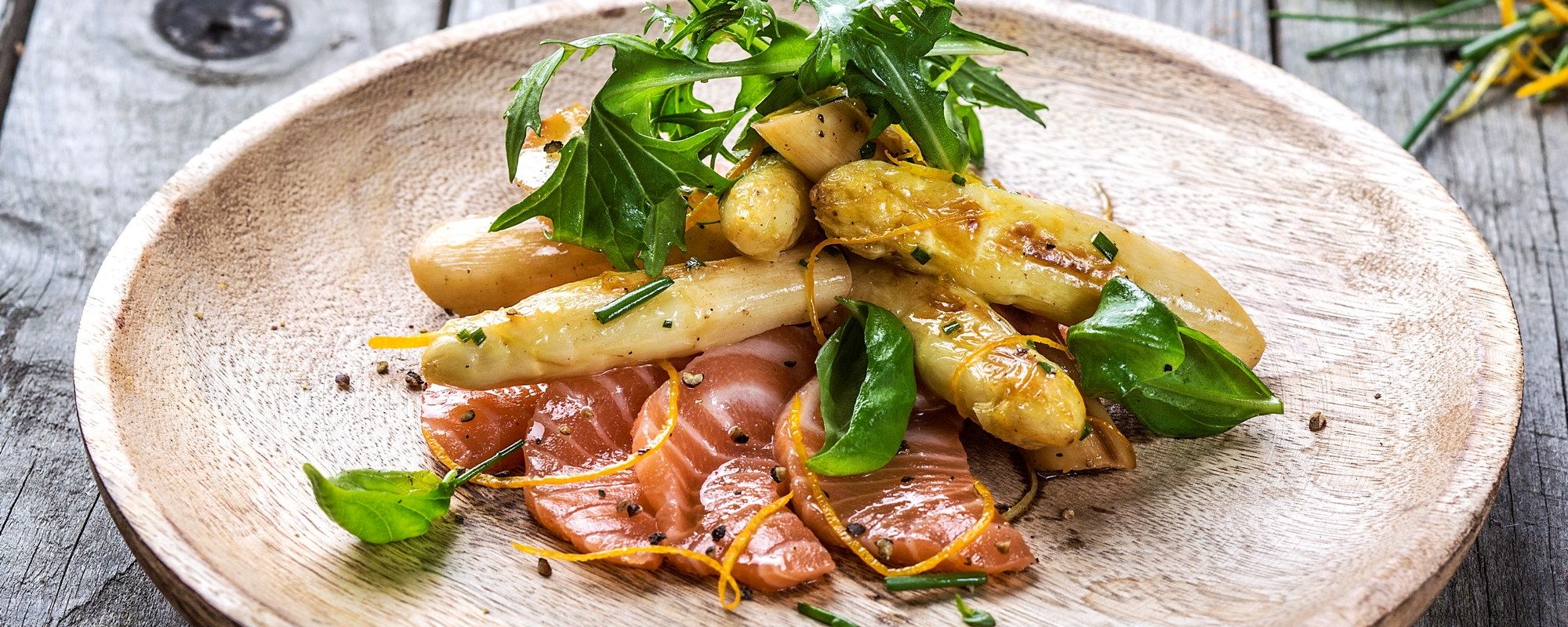 Små hvite asparges med laks og sitrus på en tallerken, pyntet med urter.