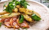 Små hvite asparges med laks og sitrus på en tallerken, pyntet med urter.