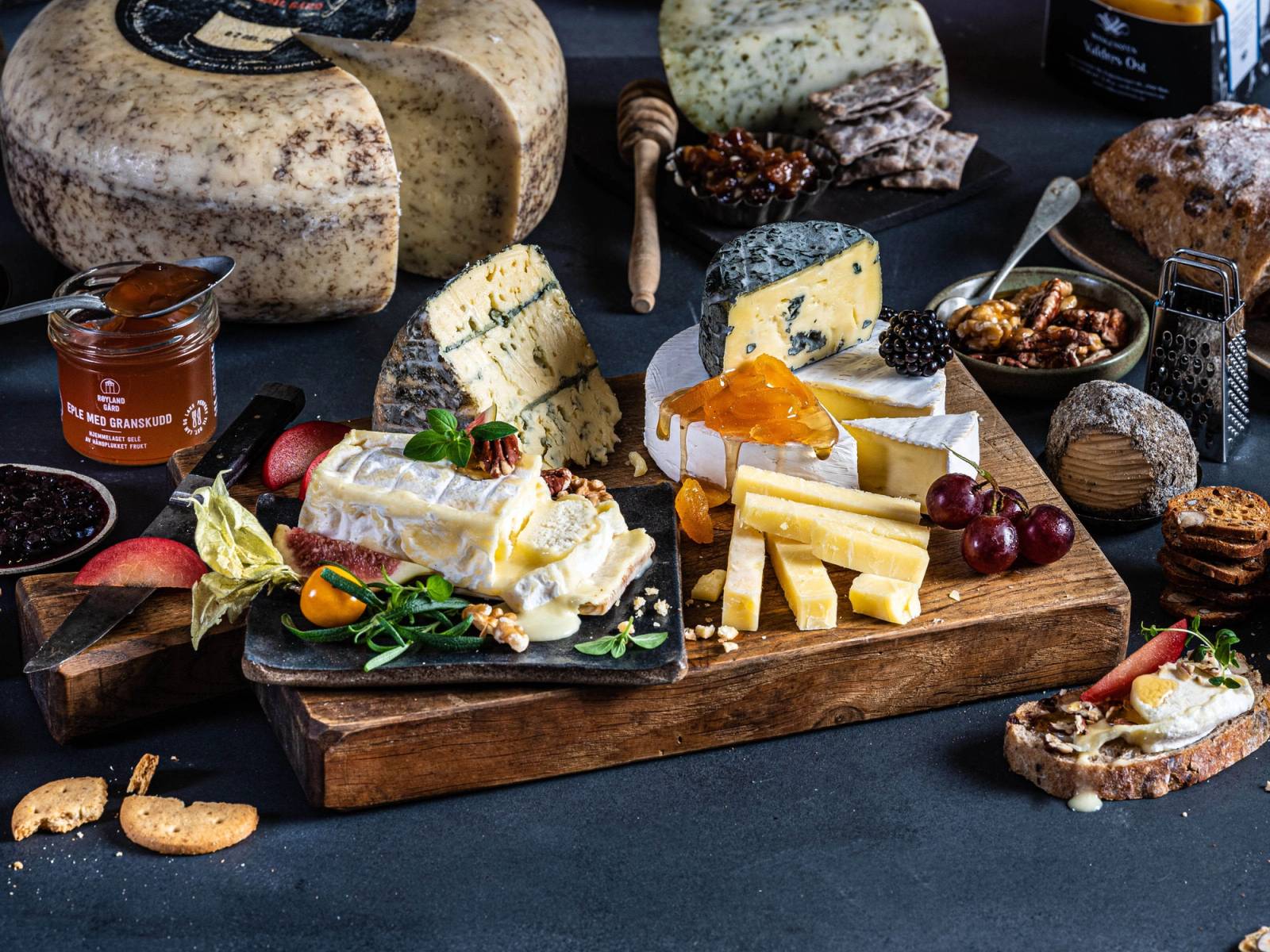 Et utvalg av ulike oster på et bord med tilbehør som druer, nøtter og kjeks.