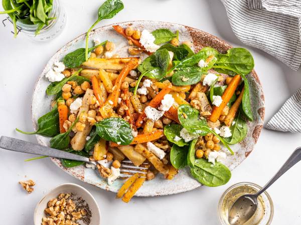En salat med ovnsbakte rotgrønnsaker, kikerter, chevreost og ferske spinatblader på en tallerken.