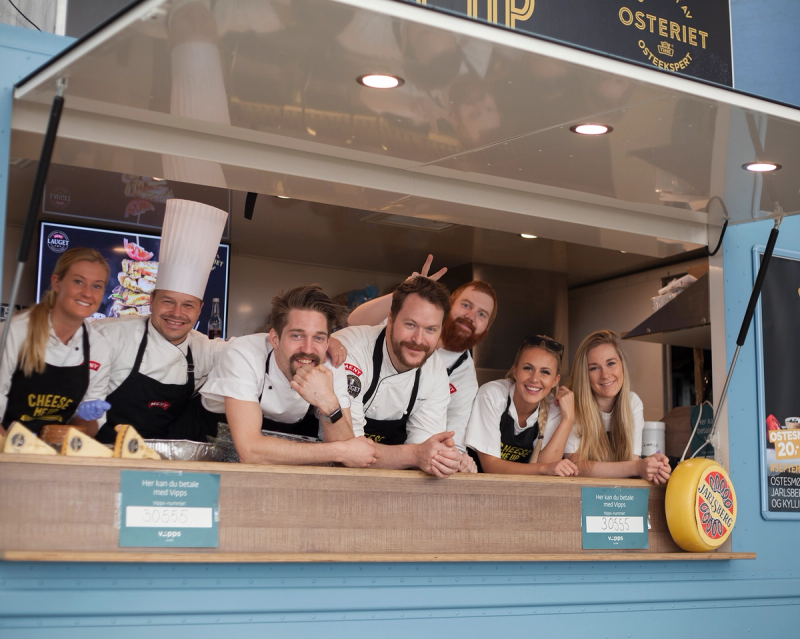 Kjøkkenpersoner står bak en matbod på Matstreif 2016, med flere personer som venter på å servere mat.