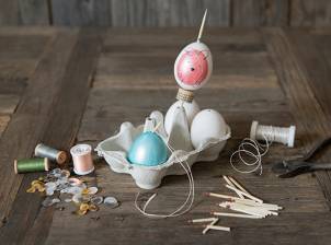 Egg som er malt og dekorert med ansikt, plassert i en eggekopp med andre egg og dekorasjoner rundt på et bord.