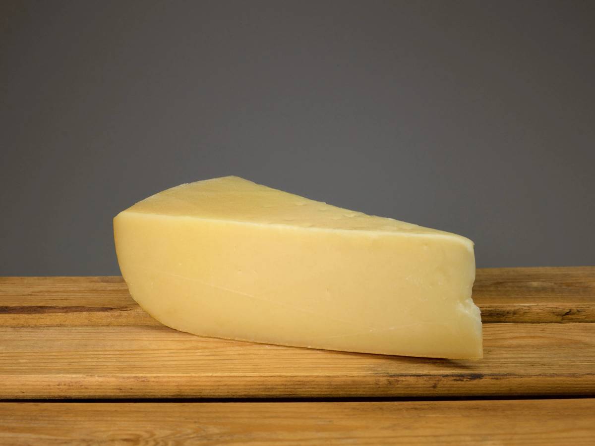 Et stykke ost med en jevn overflate og lys gul farge, plassert på en trebordflate.