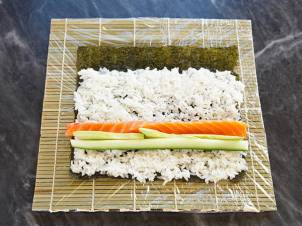 Rull med sushi med laks, agurk og ris på et bambusmatte, klar til å rulles sammen.