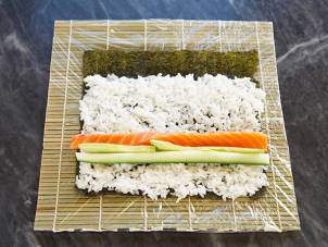 Rull med sushi med laks, agurk og ris på et bambusmatte, klar til å rulles sammen.