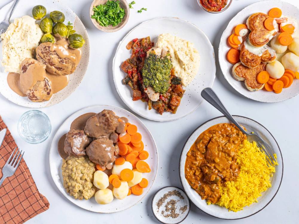 Dagens middag med ulike retter på flere tallerkener, inkludert kjøtt, grønnsaker og ris, på et hvitt bord.