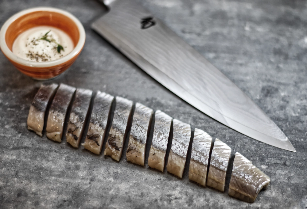 En skåret fisk på en tallerken med en kniv ved siden av, plassert på en mørk treflate.