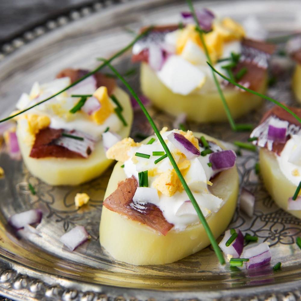 Potet med sild pyntet med hakket rødløk, egg og gressløk på et sølvfat.