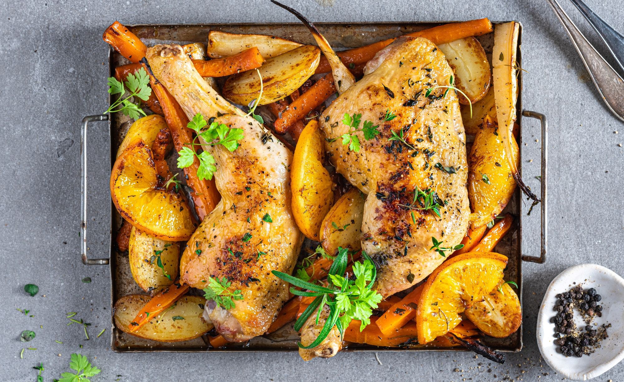 Ovnsbakte kyllinglår med poteter, gulrøtter og sitronbåter, pyntet med frisk persille, på en metallrist.