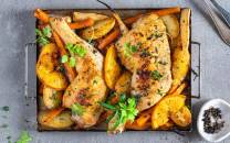 Ovnsbakte kyllinglår med poteter, gulrøtter og sitronbåter, pyntet med frisk persille, på en metallrist.