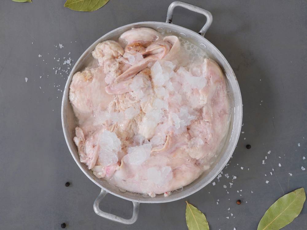 Frossen skrei torsk som ligger i en stor gryte med is og vann, klar for tilberedning.