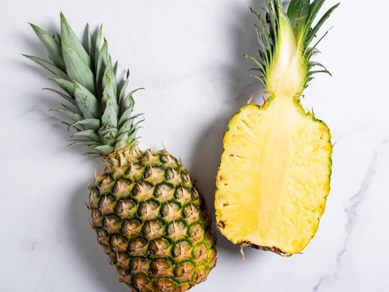 En hel og en halvt oppskåret ananas på en hvit bakgrunn.