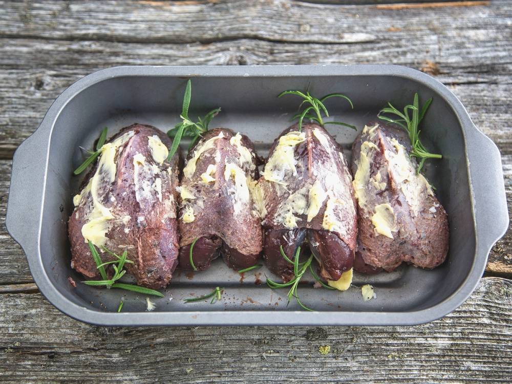 Fire rå rypefileter med urter og smør i en stekepanne på et trebord