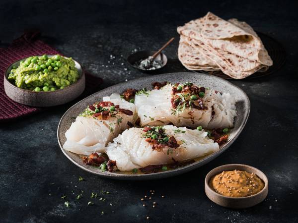 Lutefisk servert med grønnsaker, flatbrød og sennep på en tallerken, klar til å spises.