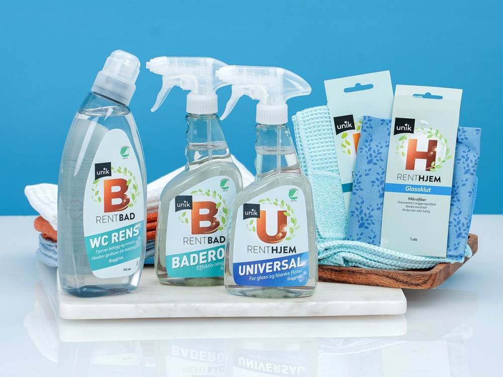 Ulike rengjøringsprodukter og vaskeklut på en hvit overflate mot en blå bakgrunn.