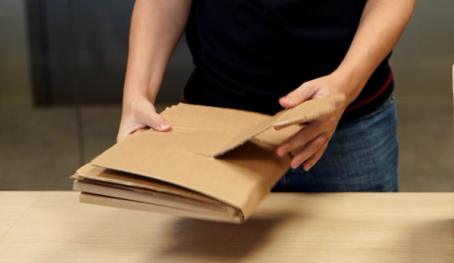 Person som holder en pappeske med flere lag av papp, klar til å åpne eller pakke ut innholdet.