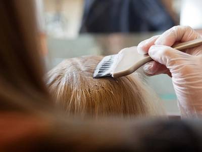 En person påfører hårfarge med en pensel på en annen persons hode, som har lyst hår.